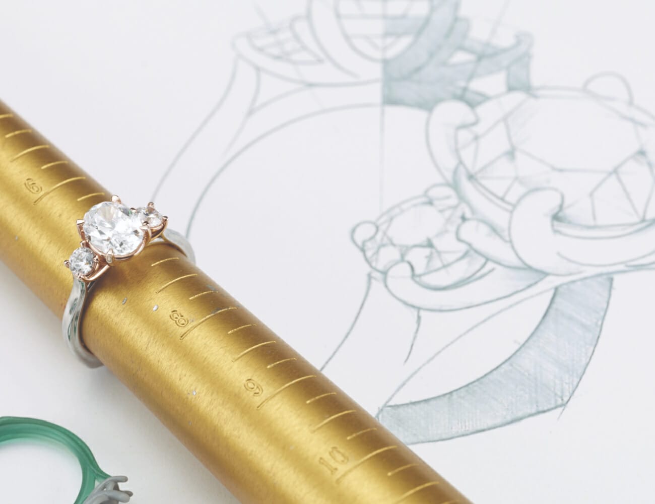A ring on a ring sizing pole, sitting beside it's bespoke drawings and designs, with the prototype setting on the left.