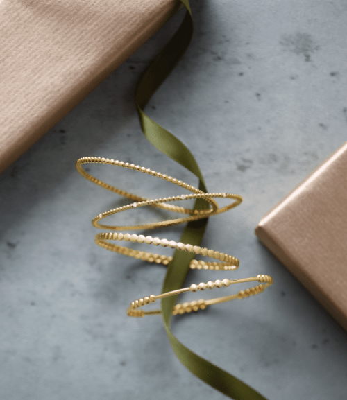 Gold bracelet jewlery with a green ribbon running through them and brown boxes in the diagonal corners