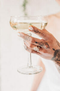 A beautiful halo setting holding diamonds on an engagement ring, on the finger of someone holding a fancy glass.
