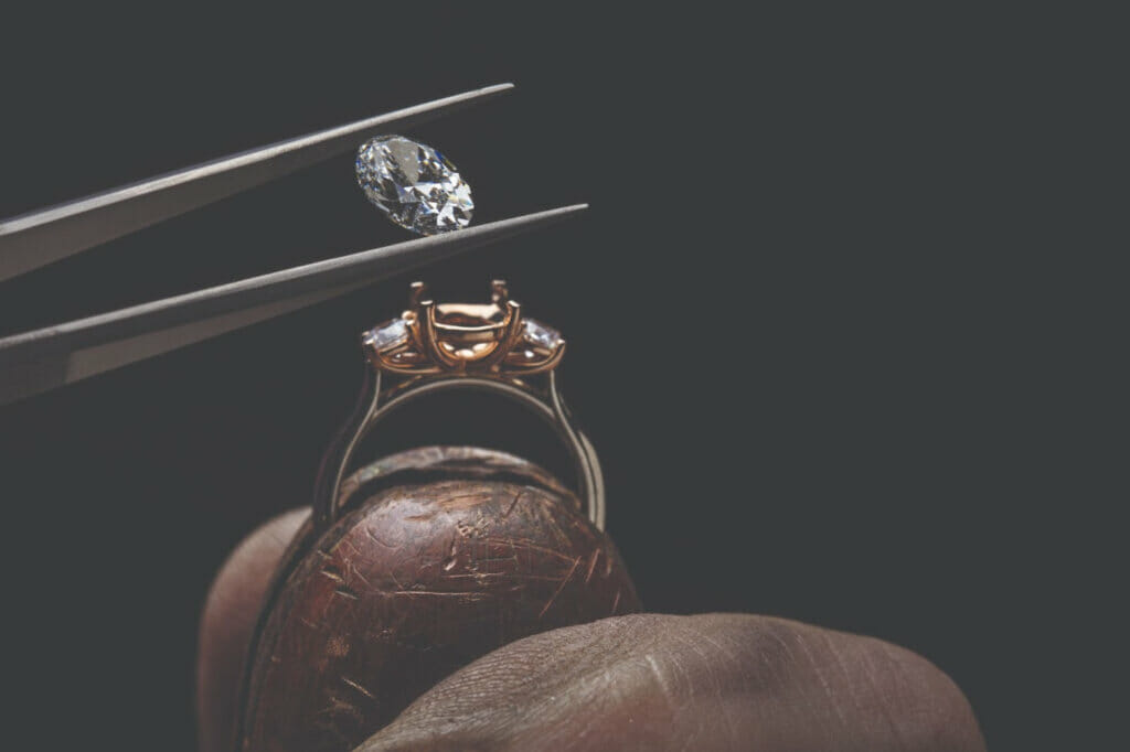 Diamond being set into a ring with tweezers against a black background