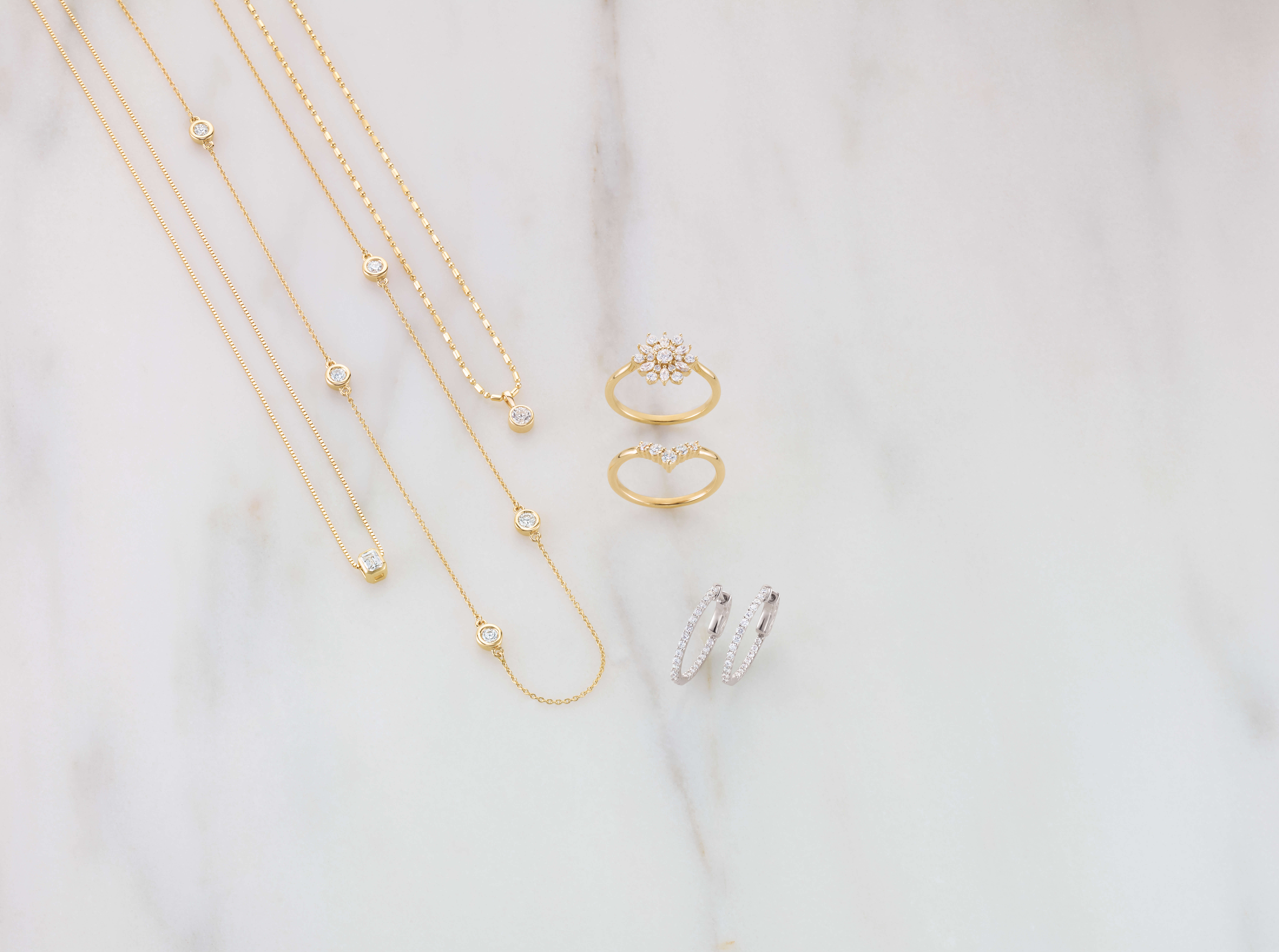 White marble counter with 3 gold chain necklaces, 2 gold diamond rings, and other diamond jewellery